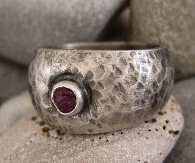 May include: A silver ring with a hammered texture and a single, round, pink gemstone set in the centre.
