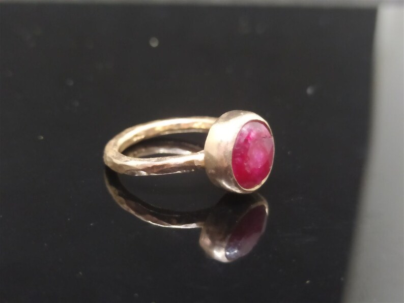 Pu&ograve; includere: Un anello d'oro con una fascia martellata e una pietra preziosa rotonda di rubino rosso.