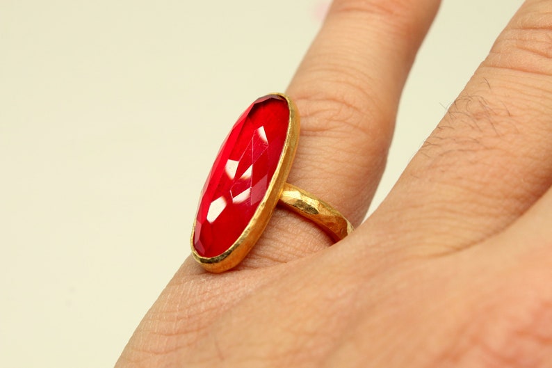 May include: A gold ring with a large, oval-shaped, faceted, red gemstone.