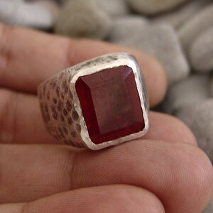 May include: A silver ring with a hammered finish and a large, square, red gemstone.