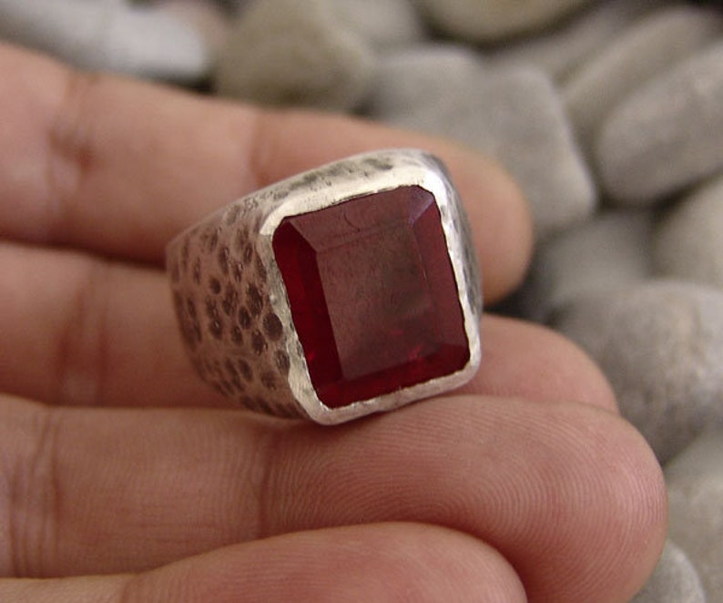 May include: A silver ring with a hammered finish and a large, square, red gemstone.
