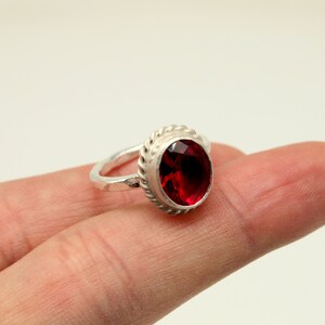 Op de afbeelding: Een zilveren ring met een rode edelsteen gezet in een touwachtig ontwerp.