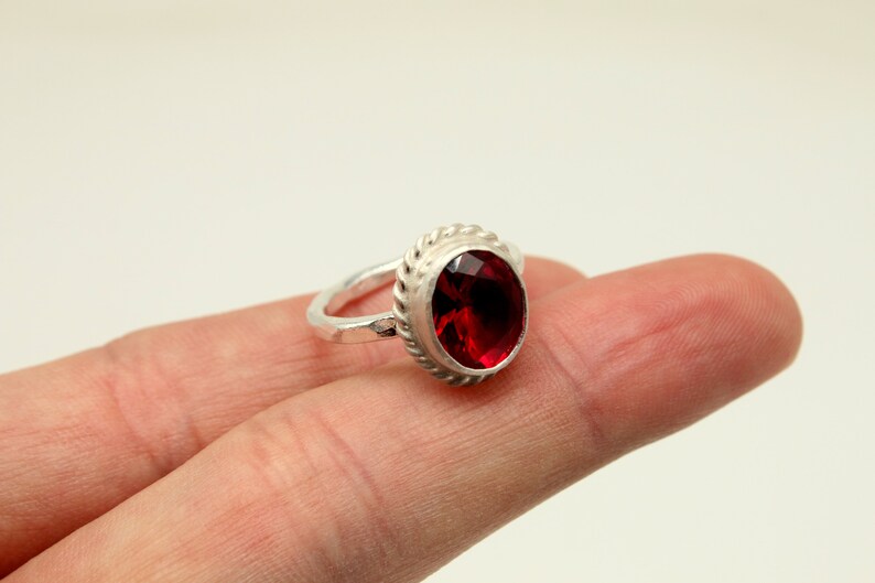 Op de afbeelding: Een zilveren ring met een rode edelsteen gezet in een touwachtig ontwerp.