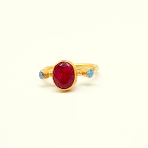 Peut inclure: Une bague en or avec une grande pierre ovale rouge et deux petites pierres bleues.