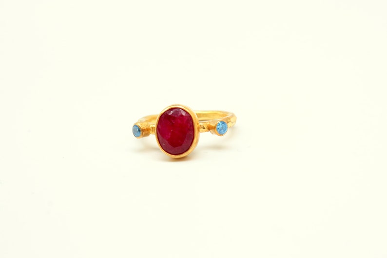 Peut inclure: Une bague en or avec une grande pierre ovale rouge et deux petites pierres bleues.