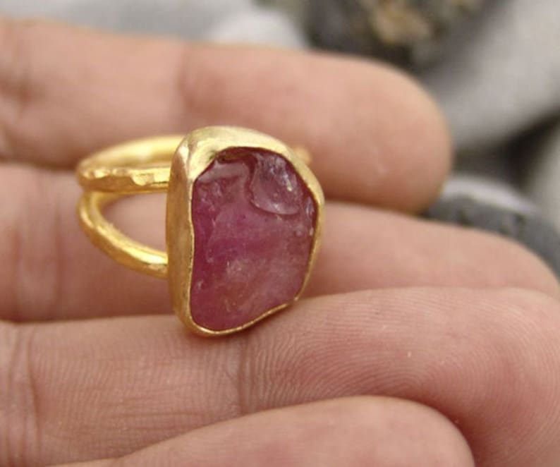 Pode incluir: Um anel de ouro com uma grande gema rosa bruta. O anel &eacute; usado em um dedo.
