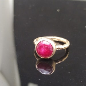 Pu&ograve; includere: Un anello d'oro con una pietra preziosa di rubino rosso brillante incastonata in una montatura a castone. La fascia &egrave; martellata e ha una finitura testurizzata.