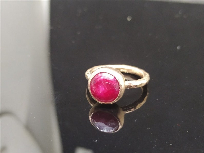 Pu&ograve; includere: Un anello d'oro con una pietra preziosa di rubino rosso brillante incastonata in una montatura a castone. La fascia &egrave; martellata e ha una finitura testurizzata.
