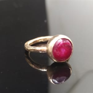 Pu&ograve; includere: Un anello d'oro con una pietra preziosa di rubino rosso. La fascia dell'anello &egrave; martellata e ha una finitura testurizzata.