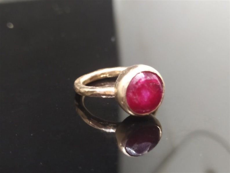 Pu&ograve; includere: Un anello d'oro con una pietra preziosa di rubino rosso. La fascia dell'anello &egrave; martellata e ha una finitura testurizzata.