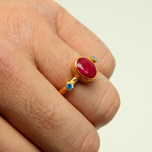 Peut inclure: Une bague en or avec une grande pierre rouge ovale et deux petites pierres bleues.