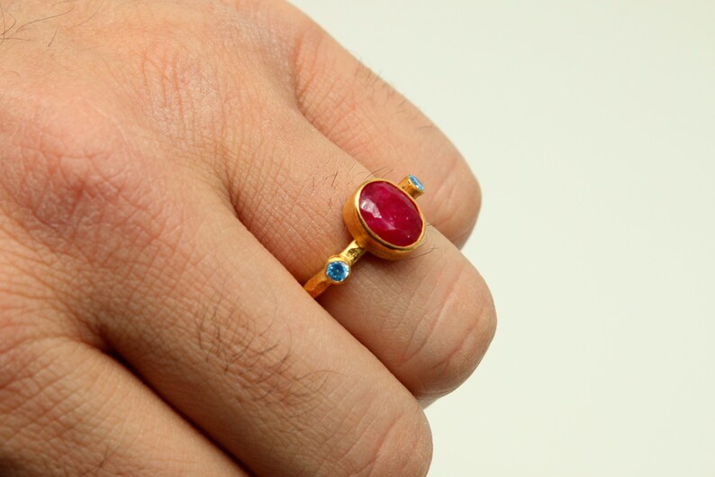Peut inclure: Une bague en or avec une grande pierre rouge ovale et deux petites pierres bleues.