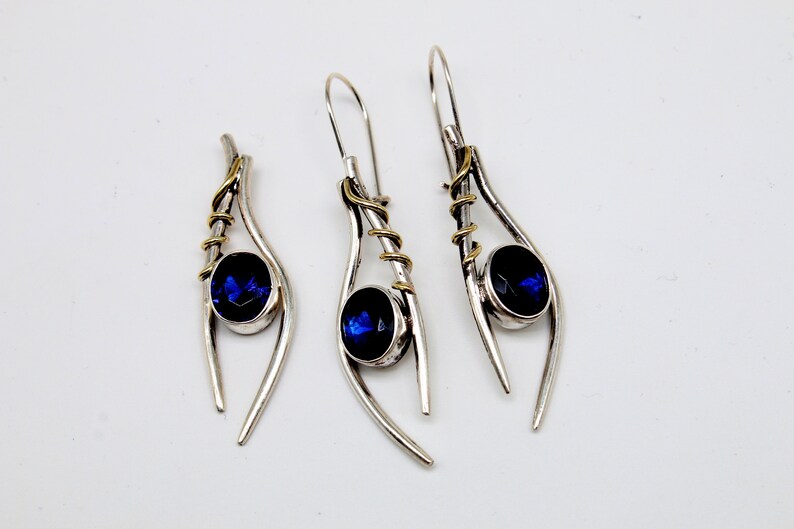 May include: A pair of silver earrings with blue gemstones and gold accents. The earrings are shaped like a teardrop with a curved wire design.
