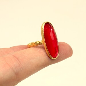 May include: A gold ring with a large, oval-shaped, red gemstone.