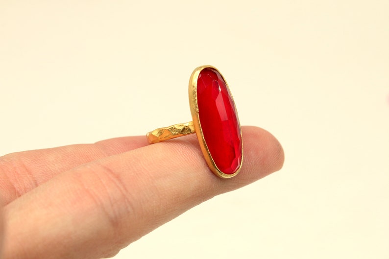 May include: A gold ring with a large, oval-shaped, red gemstone.