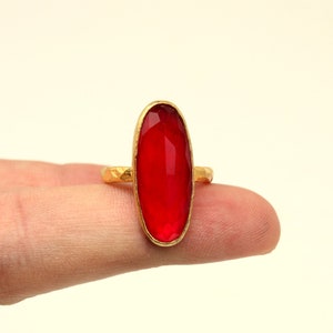 May include: A gold ring with a large, oval-shaped, red gemstone.