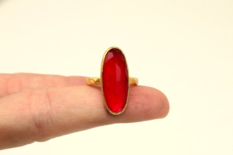 May include: A gold ring with a large, oval-shaped, red gemstone.