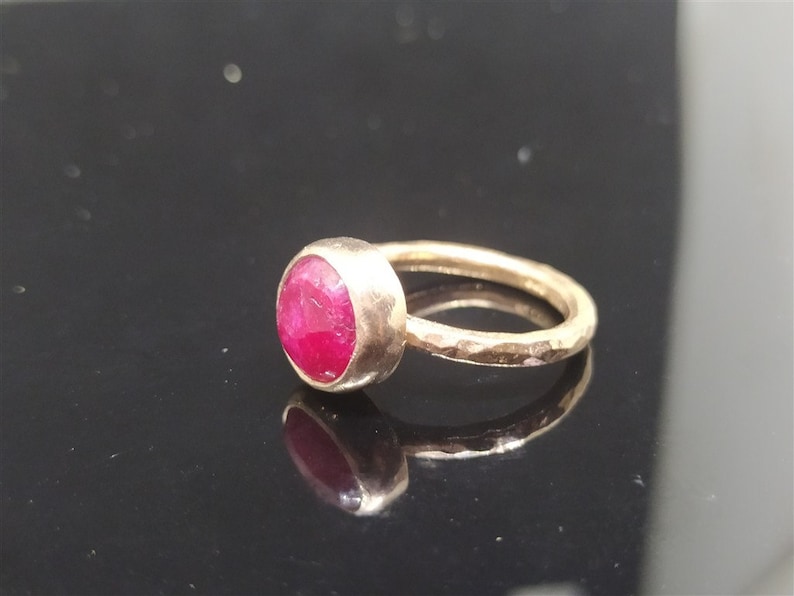 Pu&ograve; includere: Un anello d'oro con una pietra preziosa di rubino rosso brillante. La fascia &egrave; martellata e ha una finitura testurizzata.