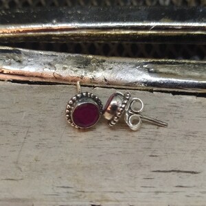 May include: A pair of silver stud earrings with a small, round, red gemstone in the center of each earring.