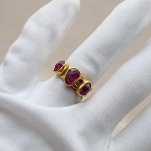 May include: A gold ring with three ruby stones set in a band. The stones are a deep red color and are set in a way that they are slightly raised from the band.