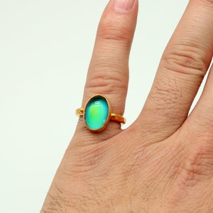 May include: A gold ring with a large oval-shaped iridescent gemstone. The gemstone is a light blue color with a hint of green.