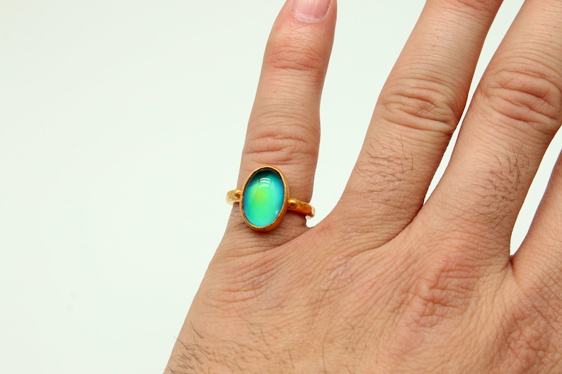 May include: A gold ring with a large oval-shaped iridescent gemstone. The gemstone is a light blue color with a hint of green.