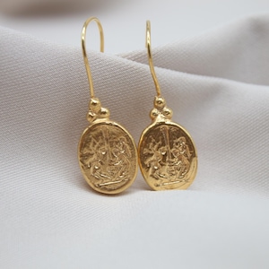 May include: A pair of gold dangle earrings with a detailed oval design featuring a raised image of two figures.