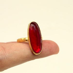 Może przedstawiać: Złoty pierścionek z dużym, owalnym, czerwonym kamieniem szlachetnym.