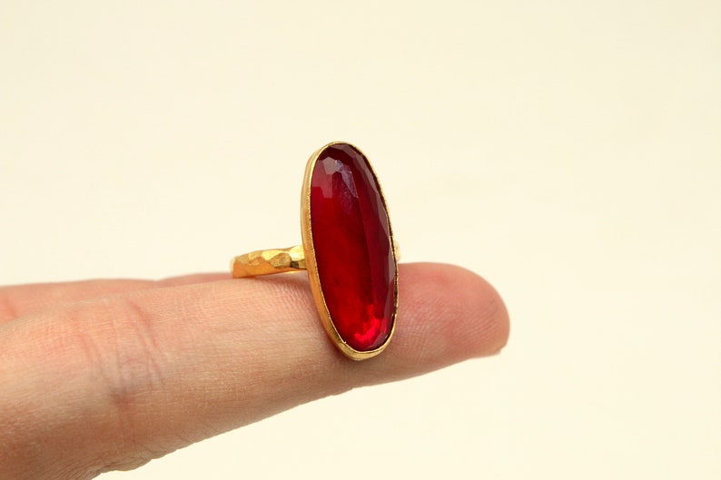 Może przedstawiać: Złoty pierścionek z dużym, owalnym, czerwonym kamieniem szlachetnym.