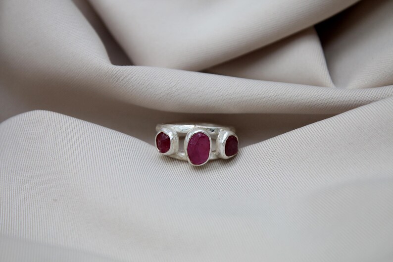 Pu&ograve; includere: Un anello d'argento con tre pietre preziose di rubino di forma ovale incastonate in una fascia testurizzata.