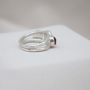 Pu&ograve; includere: Un anello d'argento con una fascia testurizzata e una singola pietra preziosa rossa.