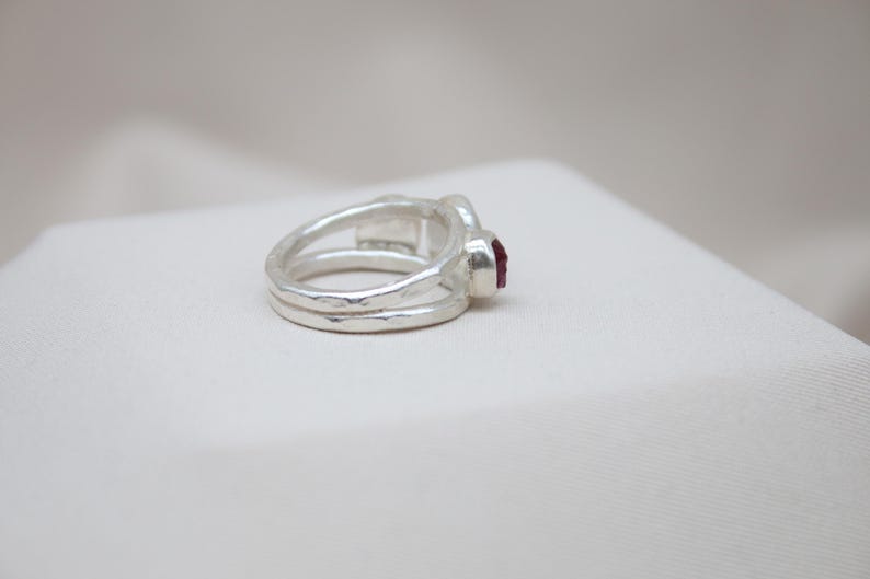 Pu&ograve; includere: Un anello d'argento con una fascia testurizzata e una singola pietra preziosa rossa.
