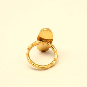 May include: A gold ring with a smooth oval-shaped stone. The ring band is textured.