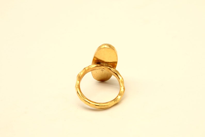 May include: A gold ring with a smooth oval-shaped stone. The ring band is textured.