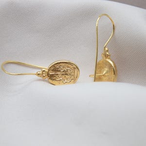 May include: A pair of gold dangle earrings with a detailed oval design. The earrings have a simple hook closure.