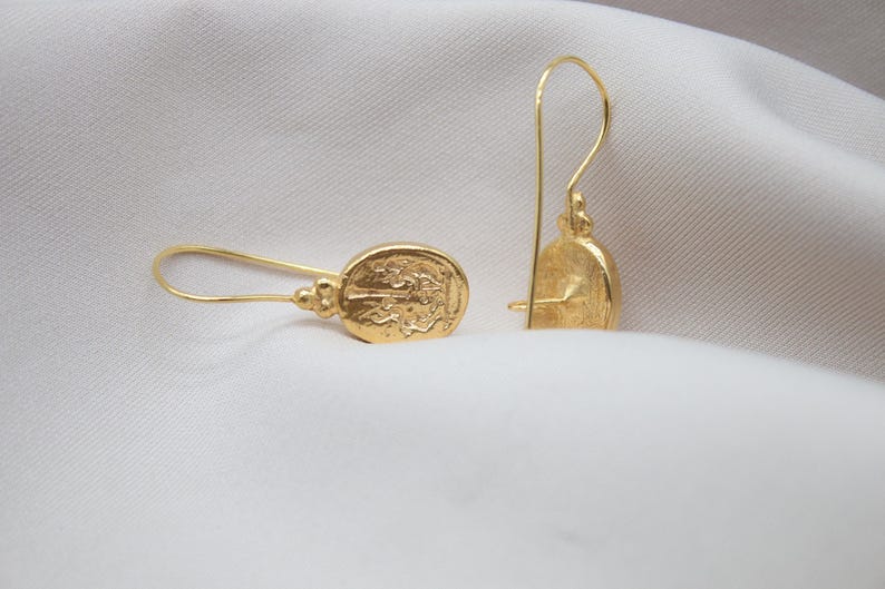 May include: A pair of gold dangle earrings with a detailed oval design. The earrings have a simple hook closure.