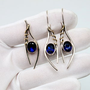 May include: A pair of silver dangle earrings with blue gemstone accents and gold wire accents.
