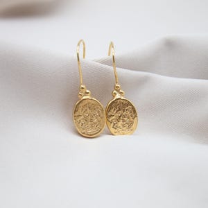 May include: A pair of gold dangle earrings with oval-shaped charms featuring intricate designs.