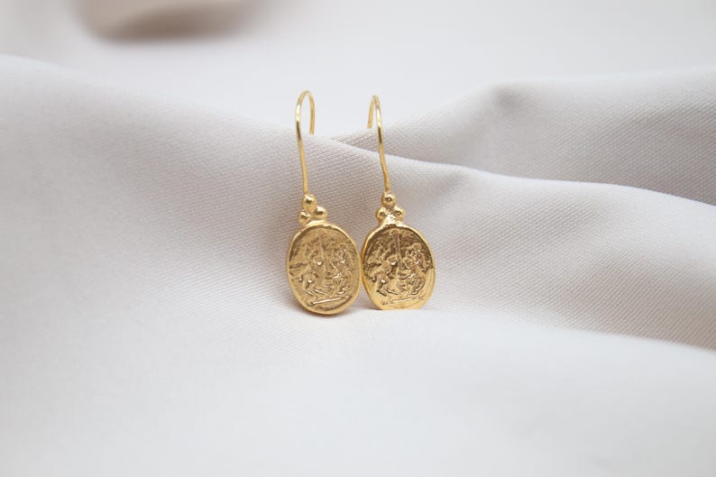 May include: A pair of gold dangle earrings with oval-shaped charms featuring intricate designs.