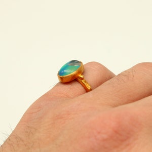 May include: A gold ring with a large oval-shaped blue and green gemstone. The ring is worn on a person's finger.