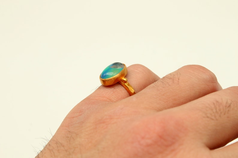 May include: A gold ring with a large oval-shaped blue and green gemstone. The ring is worn on a person's finger.