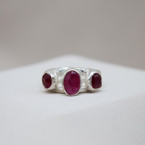 Pu&ograve; includere: Un anello d'argento con tre pietre preziose di rubino di forma ovale incastonate nella fascia.