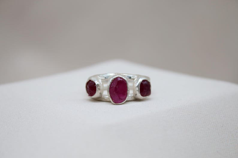 Pu&ograve; includere: Un anello d'argento con tre pietre preziose di rubino di forma ovale incastonate nella fascia.