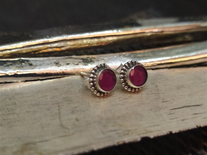 May include: A pair of silver stud earrings with small, round, dark pink gemstones set in a beaded bezel.
