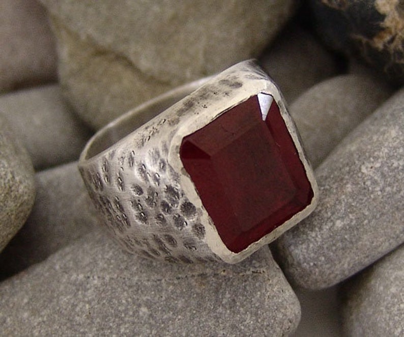 May include: A silver ring with a textured band and a large, dark red gemstone.