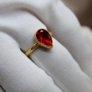May include: A gold ring with a teardrop-shaped red gemstone.