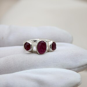 Pu&ograve; includere: Un anello d'argento con tre pietre preziose di rubino di forma ovale incastonate nella fascia.