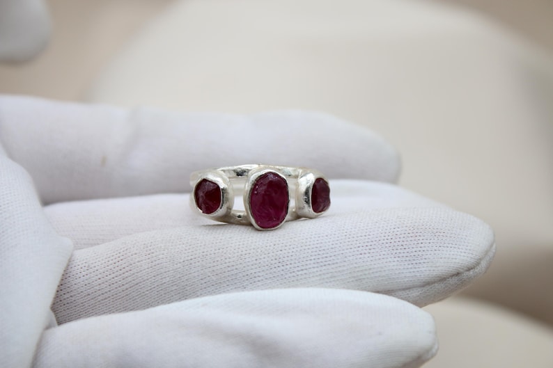 Pu&ograve; includere: Un anello d'argento con tre pietre preziose di rubino di forma ovale incastonate nella fascia.