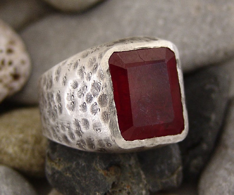 May include: A silver ring with a hammered texture and a large, rectangular, dark red gemstone.