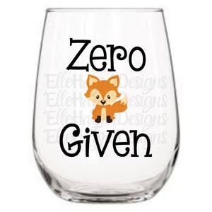 以下が含まれることがあります： 黒い文字で「Zero Given」という言葉が入った透明なステムレスワイングラス。オレンジと茶色の毛皮の漫画のキツネが言葉の間に配置されています。グラスは空です。